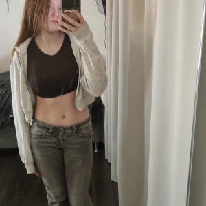 Grå croppad huvtröja från H&M Divided - Säljer en grå croppad huvtröja från H&M Divided. Tröjan har dragkedja framtill och långa ärmar. Perfekt för en avslappnad stil.