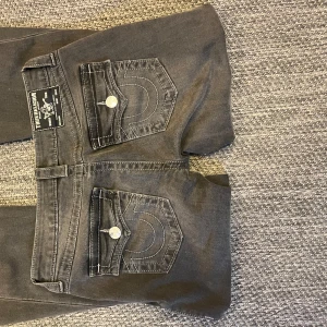 Svarta jeans från True Religion - Snygga svarta jeans från True Religion med ikoniska bakfickor och kontrastsömmar. De har en klassisk femficksdesign och knappar med logotyp. Perfekta för en stilren look.