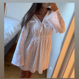 Vit klänning från NA-KD - Säljer en söt vit klänning från NA-KD med broderade detaljer och knytning i midjan och vid brösten. Orginalpris 599kr, aldrig använd. 
