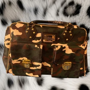 Y2k väska - Super cool militär mönstrad väska med leopard mönster på insidan❤️den är ifrån märket paul’s boutique❤️ Hand tagen har de tyvärr låssnat lite färg på men annars har den inga defekter❤️ den är 39cm lång, 24 cm hög och 15 cm bred:) de är bara stt skriva om det är några frågor😚