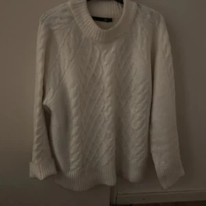 Vit stickad tröja - Säljer en mysig vit stickad tröja. Tröjan har ett klassiskt flätmönster och långa ärmar med ribbstickade muddar. Perfekt för kyliga dagar!