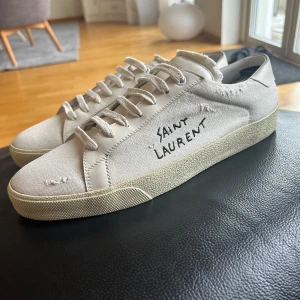Saint Laurent skor - ⚠️!!!FRAKTAR BARA VIA POSTNORD!!!⚠️Snygga vita sneakers från Saint Laurent med handskriven logga på sidan. Skorna har en klassisk design med snörning och en bekväm sula. Perfekta för en stilren look.