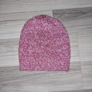 Rosa stickad mössa - Säljer en mysig rosa stickad mössa med ribbad kant. Perfekt för kyliga dagar och ger en skön passform. Den melerade hemmastickade.