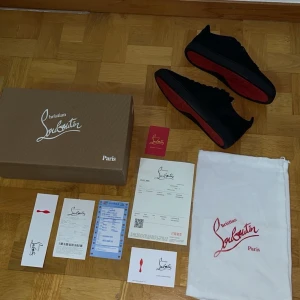 Christian Louboutin  - Snygga svarta sneakers från Christian Louboutin med den ikoniska röda sulan. Skorna har en stilren design med snörning och är tillverkade i mocka. Perfekta för den som vill ha en lyxig touch i vardagen.