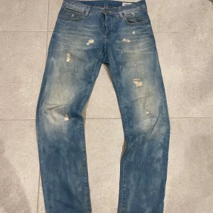 Blå jeans från G-Star - Säljer ett par blå jeans från G-Star med slitna detaljer och en klassisk femficksdesign. Jeansen har en knappgylf och är tillverkade i denim. Perfekta för en avslappnad stil. 31W 34L. Bilder på och mått kan fås vid intresse.