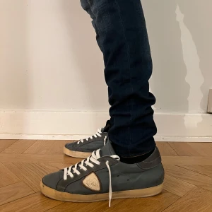 Grå sneakers med vita detaljer - Stilrena Philippe model skor med vita snören och mycket bra skick. Skorna kommer med låda. Skorna har inga defekter men lite häldrag på höger skon, men det märks inte. Om du är intresserad och undrar något  eller har frågor är det bara att fråga. Ny pris - 4000kr.