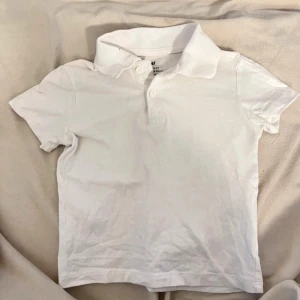 Vit pikétröja från H&M barn - Säljer en klassisk vit pikétröja från H&M i storlek EUR 92. Tröjan har korta ärmar och en krage med knappar framtill. Perfekt för en stilren och avslappnad look. Liten svart prick på krage, vet ej om det går bort 