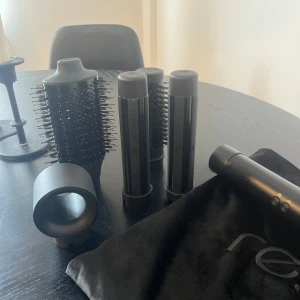 Svart hårstylingverktyg med tillbehör - Säljer ett svart hårstylingverktyg med flera tillbehör, inklusive olika borsthuvuden och cylindrar för varierad styling. Perfekt för att skapa volym och lockar. Kommer med en praktisk förvaringspåse. ordinarie pris 1699kr