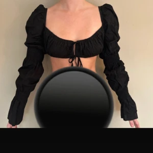 Svart långärmad blus med knyt - Svart blus med långa puffärmar och knytning framtill. Den har en smickrande fyrkantig urringning och är perfekt för en stilfull look. Passar bra till både jeans och kjol.