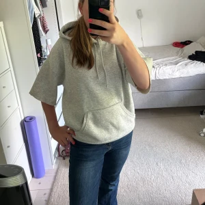 Grå hoodie med kort ärm och huva - Grå hoodie med korta ärmar, har en liten fläck på ärmen som man ser på den fjärde bilden.