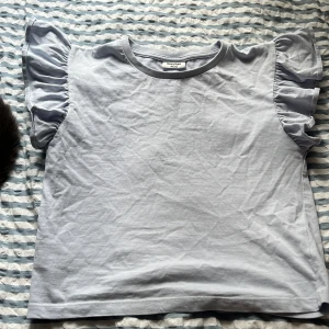 Ljusblå volangtopp från Kappahl - Supersöt ljusblå topp från Kappahl med volangdetaljer på ärmarna. Fläcken grå förmodligen bort i tvätten och syns inte när man har den på. 