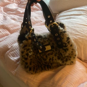 Väska  - Säljer en fluffig handväska med leopardmönster och svarta, breda handtag i skinnimitation med coola metalldetaljer och spännen. Pris kan diskuteras 