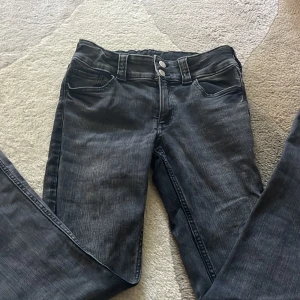 Svarta bootcut jeans  - Snygga svarta bootcut jeans från H&M med låg midja och justerbar midja. Jeansen har dubbla knappar fram, klassiska fickor och bakfickor med lock och knapp. 