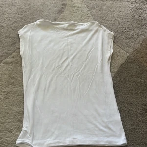 Vit ärmlös topp - Enkel och stilren vit topp från Lager157 i storlek XS. Modellen är ärmlös med rak halsringning och tight passform. Gjord i mjukt och lätt bomullsmaterial. Tröjan har inga fläckar och sparsamt annvänd. 
