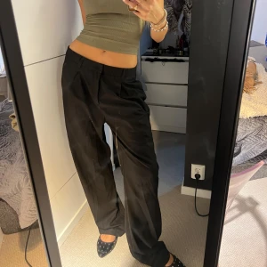 Svarta lowwaist kostymbyxor Design by Si - Svarta kostymbyxor från Design by Si i storlek M. Byxorna har en loose och wide passform med låg midja och snygga pressveck framtill. Tillverkade i en mjuk blandning av polyester och viskos som ger ett dressat men bekvämt intryck. Älskar dessa men tyvärr är de lite för stora på S, gillar du riktigt baggy är dessa för dig!