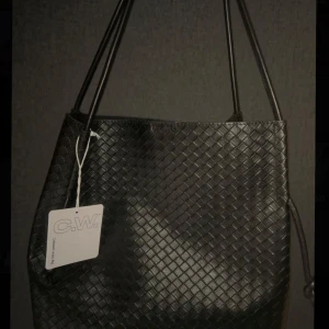 Svart Annie axelväska från Carin Wester - Säljer en helt ny svart Annie axelväska från Carin Wester. Väskan har ett snyggt flätat mönster och är gjord i skinnimitation. Den har långa axelband och minimalistisk design som passar till allt. Perfekt för dig som vill ha en stilren och trendig väska med plats för det viktigaste. Köpt för 699kr aldrig använd 