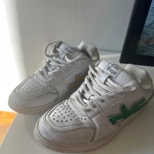 Lost Boys vita sneakers med utbytbara detaljer - Unika vita sneakers från Lost Boys med perforerad tå och utbytbara sidodetaljer i form av färgglada vapen i grönt, gult, blått, rött och marinblått. Skorna har snörning, platt sula och coolt mönster under sulan. Perfekt för dig som vill sticka ut med din egen stil. Storlek 42 men är lite små i storleken, passar mer som 40-41, skriv privat så skickar jag fler bilder💕 nypris är lite över 2000kr