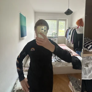 Svart långärmad tröja från Vans - Svart långärmad tröja från Vans med färgglada regnbågar tryckta på ärmen, bröstet och en stor på ryggen. Tröjan har en klassisk passform och är gjord i mjuk bomull, perfekt för dig som gillar streetstyle och färgglada detaljer.