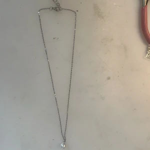 Silverhalsband med vit pärla -  Rostfritt stål, handgjord. Stilrent halsband i silverfärgad kedja med en droppformad vit pärla som hänge. Perfekt för dig som gillar minimalistiska smycken med en elegant touch. Passar till alla outfits och ger en klassisk vibe.