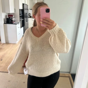 Beige stickad tröja - Mysig beige stickad tröja med v-ringning och långa ärmar. Tröjan har en loose passform och breda ribbade muddar vid ärmslut och nederkant. Perfekt att slänga på sig när det är kyligt ute. 