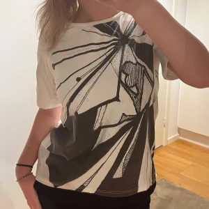 Vit t-shirt med grafiskt tryck Tiger of Sweden jeans - Vit t-shirt från Tiger of Sweden Jeans med ett stort svart grafiskt tryck på framsidan. Klassisk rund halsringning och korta ärmar. Skön passform och i mjukt material, perfekt för en cool och avslappnad stil. Axelbredd: 43cm. Längd: 63cm. Byst: 45cm. 