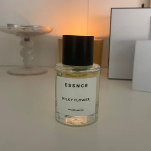 ESSNCE Milky Flower Eau de Parfum - Parfymen Milky Flower från ESSNCE kommer i en stilren, rund glasflaska med svart lock. Doften är blommig och mjuk, perfekt för dig som gillar fräscha och krämiga toner. Flaskan har en minimalistisk vit etikett med svart text och rymmer Eau de Parfum. Endast använd 2 gånger. Så inprincip oanvänd.