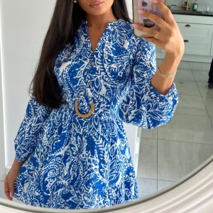 Blåvit kortklänning med bälte - Superfin blåvit kortklänning med paisleyinspirerat mönster och markerad midja med snyggt bälte. Klänningen har långa ärmar, v-ringning med knappar och luftig passform. Perfekt för sommarens alla tillfällen!