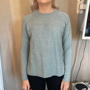 Ljusgrå stickad tröja med slits - Enkel och stilren ljusgrå stickad tröja med rund halsringning och lång ärm. Tröjan har en liten slits i nederkanten på ena sidan som ger en snygg detalj. Perfekt för lager-på-lager och chill dagar.