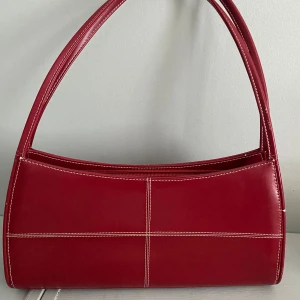 Röd axelväska i skinn med kontrastsömmar - Snygg röd axelväska i skinn med vita kontrastsömmar köpt i London på vintage butik 