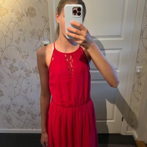 Röd spetsklänning från Vero Moda  - Supersnygg röd klänning från Vero Moda i storlek XS. Klänningen har spetsdetaljer fram och i sidorna, smala axelband och markerad midja. Den är ärmlös och har en liten öppning i ryggen. Perfekt för dig som vill sticka ut med en färgstark look!