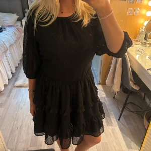 Svart klänning från Bik Bok - Supersöt svart kortklänning från Bik Bok med volangkjol, prickig struktur och trekvartsärmar. Klänningen har öppen rygg med knyt och är gjord i ett lätt, transparent material som ger en luftig känsla💞