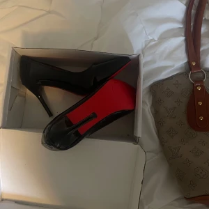 Svarta lackpumps med röd sula - Snygga svarta pumps i lack med ikonisk röd sula och spetsig tå. Skorna har hög klack och en elegant, tidlös design som verkligen sticker ut. Perfekta för dig som vill ha en klassisk men ändå edgy look. Oanvända!