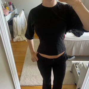 Svart croppad topp med knyt i ryggen - Säljer en svart croppad topp med halvlånga ärmar och öppen rygg som knyts med en stor rosett. Toppen har en enkel och stilren design, perfekt för att ge en cool touch till din outfit. Gjord i mjuk bomull för skön känsla.