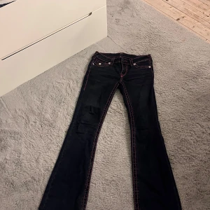 True Religion jeans med rosa sömmar - Mörkblå jeans från True Religion med snygga rosa kontrastsömmar och ikoniska bakfickor med broderi. Perfekt för dig som vill sticka ut med detaljer.