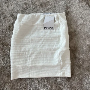 Vit ribbad kjol från INSIDE - Säljer en stilren vit kortkjol från INSIDE med diskret ribbad struktur. Kjolen har en enkel och clean design som är lätt att matcha med olika toppar. Perfekt för dig som gillar minimalistisk stil.