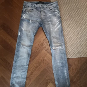Amiri jeans - Säljer ett par ljusblå skinny jeans från Amiri med slitna detaljer, hål på knät och coola slitningar framtill. Jeansen har klassisk femficksdesign och är tillverkade i mjukt denim. Perfekta för dig som gillar streetstyle och vill sticka ut.