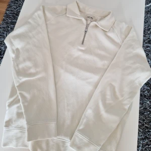Vit half zip tröja från East West - Säljer en stilren vit tröja från East West i storlek M. Tröjan har en klassisk krage och half zip-dragkedja framtill. Ribbade muddar vid ärmslut och nederkant. Perfekt för lager-på-lager och enkel att matcha.