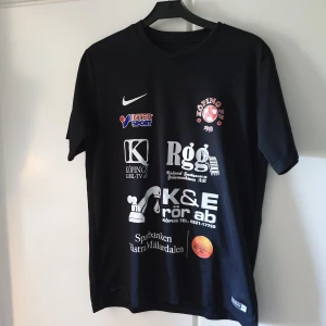 Köping FF matchtröja Nike svart nr 25 - Svart fotbollströja från Nike med Köping FF-logga och flera sponsortryck på framsidan. Stort vitt nummer 25 på ryggen och klubbnamn ovanför. Klassisk sportdesign i funktionsmaterial, perfekt för dig som gillar fotboll och vill sticka ut på planen. Barnstorlek: 158-170cm, 13-15 år. Plagget har befunnit sig i samma hem som en katt. Så kan följa med något enstaka katthår. 