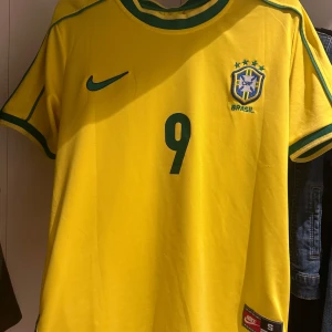 Brasilien Ronaldo 9 Nike fotbollströja - Gul Brasilien fotbollströja från Nike med gröna detaljer, nummer 9 och Ronaldo på ryggen. 