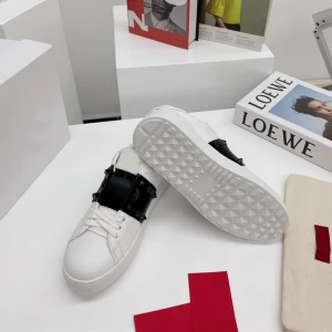 Valentino Rockstud sneakers vit/svart - Snygga vita Valentino Rockstud sneakers med svart band över vristen och ikoniska nitar runt hälen. Skorna har rund tå, platt sula och är gjorda i skinn. Perfekt för dig som vill sticka ut med en clean men edgy look.