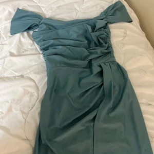 Ljusblå långklänning med offshoulder - Supersnygg ljusblå långklänning med offshoulder och draperad överdel. Klänningen har en elegant slits och fina detaljer vid axlarna. Perfekt för dig som vill sticka ut med en stilren och modern look. Använd bara två gånger men den ser fortfarande sol helt ny. 