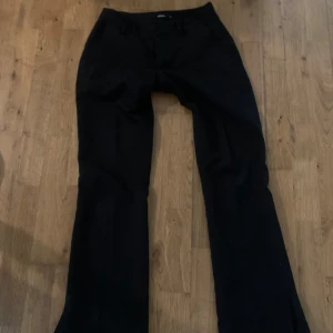 Svarta lågmidjade bootcut kostymbyxor BikBok - Svarta kostymbyxor från BikBok i klassisk bootcut-modell. Byxorna har fickor fram, en snygg, stilren look. Perfekta för dig som gillar en tidlös och clean stil. Med slits nertill.
