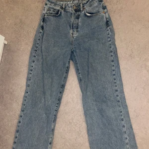 Blå wide jeans med hög midja - Säljer ett par klassiska blå jeans med hög midja och wide fit. Jeansen har raka ben, fem fickor och knäppning med knappar. Materialet är robust denim i bomull. Perfekta för en avslappnad och trendig look.