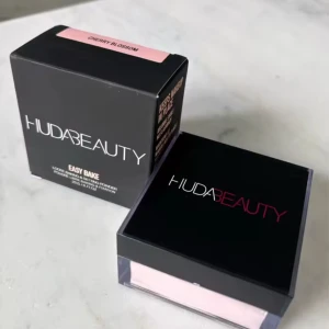 Huda Beauty Easy Bake Cherry Blossom - Huda Beauty Easy Bake Loose Baking & Setting Powder i nyansen Cherry Blossom. Ett löspuder med en ljusrosa ton, perfekt för att fixera sminket och ge en mjuk, matt finish. Kommer i en stilren svart och transparent burk med skruvlock.
