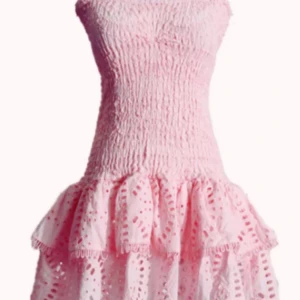 Rosa kortklänning med volanger - Supersöt rosa kortklänning med smockad överdel och volangig kjol. Klänningen är axelbandslös och har broderade detaljer i kjolen. Köpt på marknad! Aldrig använd, står ingen storlek men är stretchig så XXS-liten M