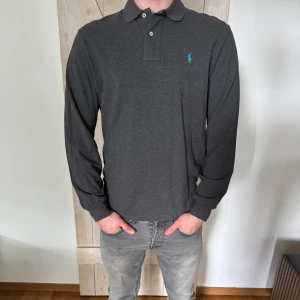 Mörkgrå långärmad pikétröja Polo Ralph Lauren - Snygg mörkgrå långärmad pikétröja från Polo Ralph Lauren. Storleken är M och skicket är bra