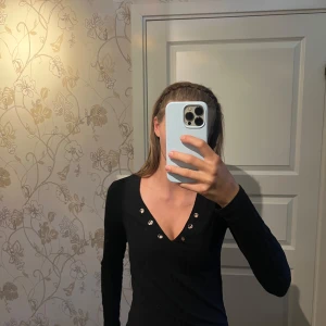 Svart ribbad tröja med nitar Crocker - Svart långärmad tröja från Crocker med ribbad struktur och coola silverfärgade nitar runt v-ringningen. Sitter tight och har en snygg passform som framhäver figuren. Perfekt till jeans eller kjol för en stilren look.