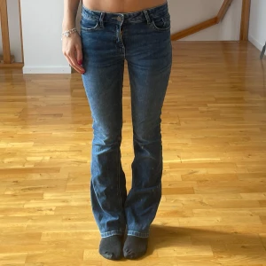 Blå bootcut jeans midwaist - Säljer ett par klassiska blå jeans med bootcut passform och midwaist. Jeansen har fem fickor, dragkedja och knapp framtill. Materialet är jeans i bomull och de har en snygg, tidlös tvätt. Perfekta till sneakers eller boots. De finns ett litet litet hål i byxorna på knä skålen men de e extremt litet å syns ej nät nan står up.