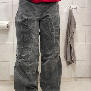 Grå baggy cargopants med detaljer - Säljer ett par grå cargopants i baggy modell med flera fickor och coola sömdetaljer. Byxorna har bred passform, D-ring och rem på sidan för extra streetkänsla. Perfekta för dig som gillar avslappnad stil och vill sticka ut lite extra.🪩⭐️