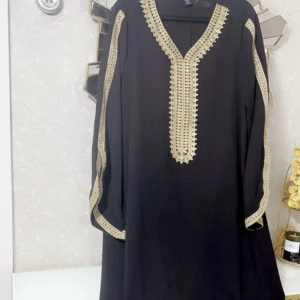 Svart arabisk klänning med guldiga detaljer - Svart arabisk klänning med snygga guldiga broderade detaljer längs v-ringningen och ärmarna. Klänningen har lång ärm och ett elegant, löst fall. Perfekt för dig som vill sticka ut med stilrena detaljer. Storleken XL✨